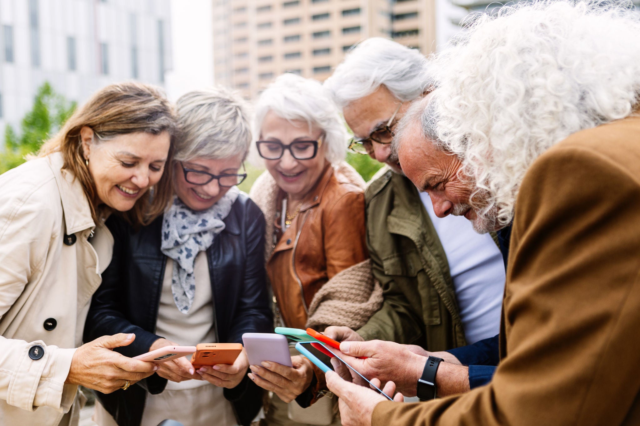Groupe de personnes retraitées qui utilisent l’appareil mobile et qui se tiennent en cercle à l’extérieur. Groupe de personnes retraitées qui utilisent l’appareil mobile et qui se tiennent en cercle à l’extérieur.